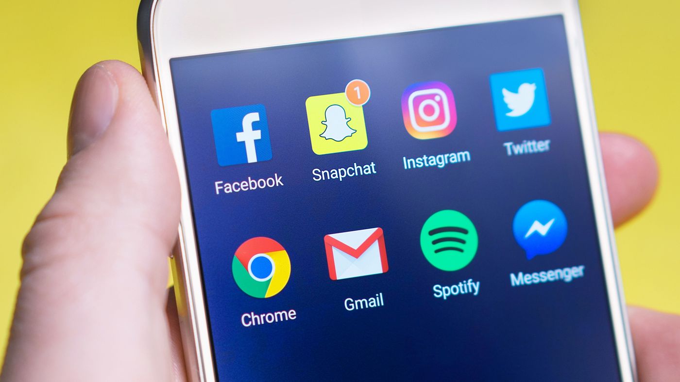 Une main tient un smartphone affichant les applications de réseaux sociaux